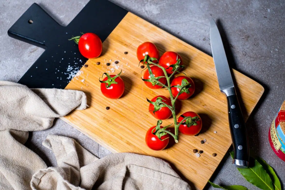Red Tomato Beside Stainless Steel Bread Knife on Brown Wooden Chopping Board